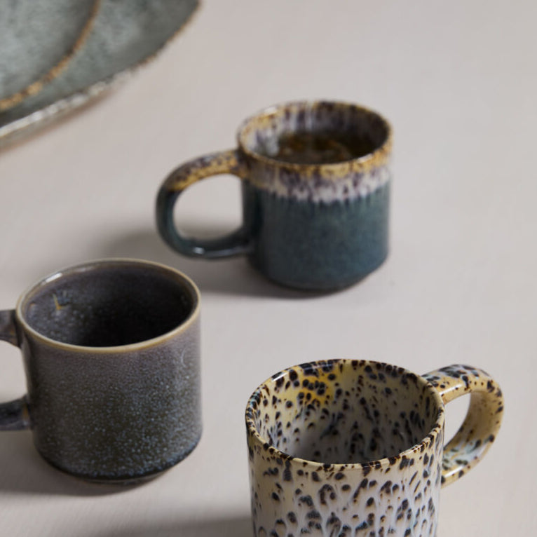 Three ceramic mugs with speckled patterns on a light surface